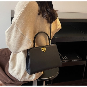Détail d'un sac à main chic en cuir noir avec fermoir rotatif doré et anse courbée