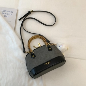 Detail of shell bag with bamboo handle, matte gray finish, and plush bird charm accessory