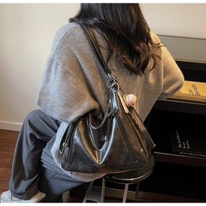 Detail of black glossy leather tote bag with side zippers and tassel decorations