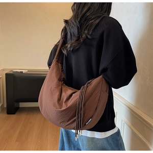 Detail of brown waffle-textured moon bag with drawstring and brand label on shoulder