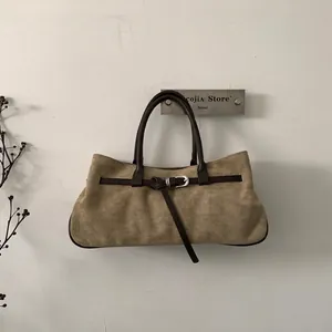 Detail of khaki suede tote bag featuring dark brown leather straps and buckle decor