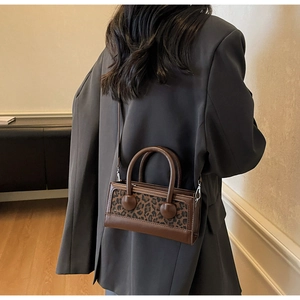 Detail view of brown leather crossbody bag with leopard print panel and ball handle hardware