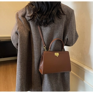 Sac fourre-tout en cuir marron avec boucle dorée porté sur un blazer en tweed gris