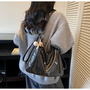 Detail of black leather hobo bag with baseball charm on a model's shoulder in soft light