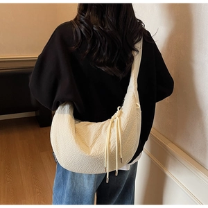 Detail of cream half-moon bag featuring textured fabric and tassels for a stylish look