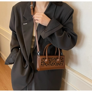 Brown leather crossbody bag with leopard print panel worn by a model in a blazer