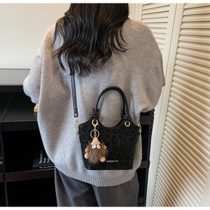 Close-up of black leopard embossed handbag with elegant plush bear charm detail