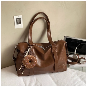 Detail of a brown leather tote bag featuring plush donut and chocolate charms for travel