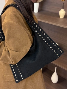 Vintage black suede tote bag with gold rivets worn by a model in a cozy setting