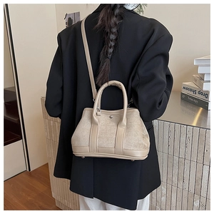 Detail of beige suede and leather tote bag featuring metal rivets and thin shoulder strap