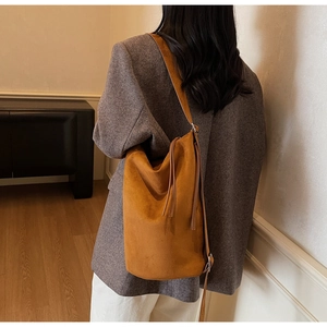Detail of a brown matte suede shoulder bag featuring a soft bucket shape and elegant tassels
