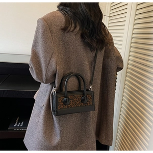 Fashionable leopard print handbag with black leather trim shown worn with a brown blazer