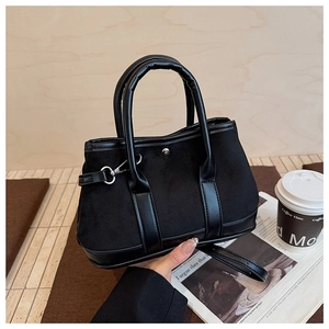 Detail of black suede tote bag with leather straps and silver hardware on a wooden table