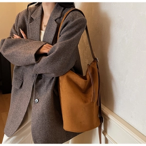 Side view of brown matte suede bucket bag with decorative fringe on a female model