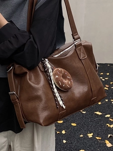 Large dark brown leather tote bag with donut charm and wide strap on model's shoulder