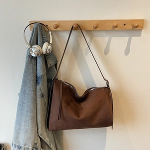Detail of dark brown suede shoulder bag with silver zipper and long tassels on hanger