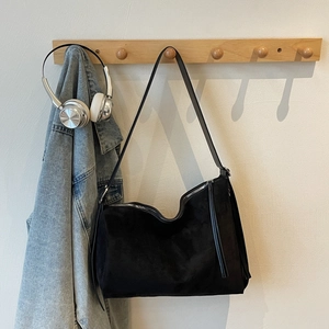 Detailed macro view of black suede hobo bag with zipper closure and slim strap on wood hook