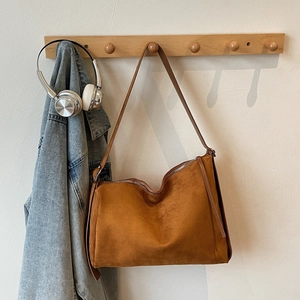 Detail of brown matte suede hobo bag with metal zipper hanging on a wooden hook rack