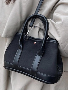Chic black canvas handbag with leather trim and shoulder strap shown on a beige coat