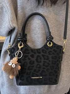 Fashionable leopard print bucket handbag with plush charm and adjustable shoulder strap