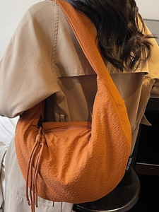 Minimalist orange half-moon crossbody bag with crinkle texture for women on a beige trench coat