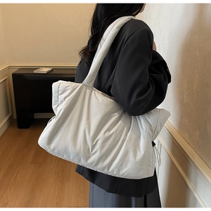 Side view of a large white quilted cloud tote bag worn over the shoulder by a model