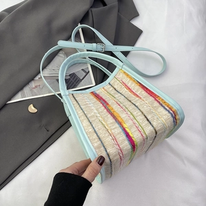 Détail d'un sac cabas en tricot crème avec anses en cuir bleu et coutures arc-en-ciel