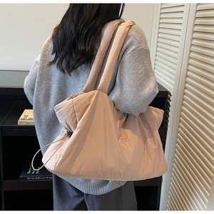 Model wearing a large quilted tote bag in soft apricot pink with drawstring detail