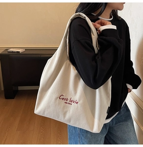 Dettaglio della borsa tote in velluto a coste crema con ricamo rosso e tracolla larga
