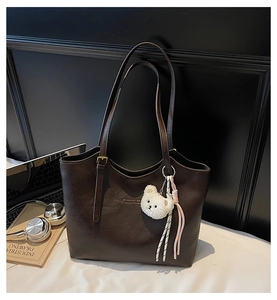 Detail of dark brown tote bag with plush bear charm and adjustable shoulder straps