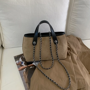 Detail view of brown suede tote bag with black leather handles on a white fabric sofa