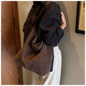 Detail view of a large vintage brown matte shoulder tote bag worn by a model in a retro setting