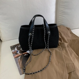 Detail of black faux suede tote bag with leather handles and silver metal chain strap