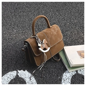 Detail of brown suede handbag featuring white contrast stitching and wooden rocking horse charm