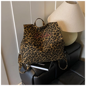 Detailed view of leopard print canvas backpack with red embroidery on a black sofa