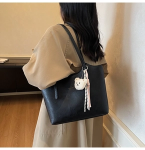 Detail view of black leather tote bag with plush bear charm and ribbon on model's shoulder