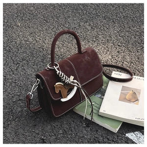 Detail of dark brown retro square bag featuring white stitching and a horse charm on street