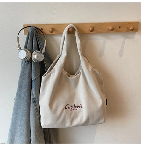 Dettaglio borsa tote in velluto a coste bianco crema con ricamo rosso su gancio in legno