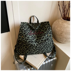 Detailed view of green leopard print canvas backpack with red embroidery on a suitcase