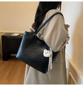 Detail of black faux leather tote with plush bear charm and striped ribbon on shoulder