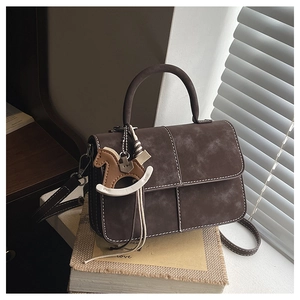 Retro brown crossbody bag with contrast stitching and leather horse charm on rustic books