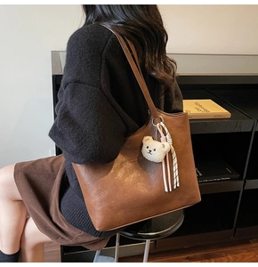 Detailed side view of a brown tote bag with a white plush bear charm and long straps
