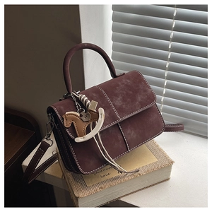 Detail of vintage red textured leather handbag with white stitching and horse charm