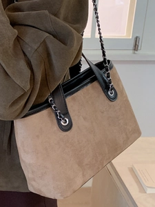 Brown suede tote bag with black chain strap shown in a cozy indoor setting