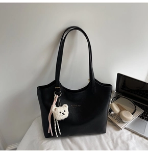 Detail of black tote bag with gold lettering, plush bear charm, and premium PU leather finish