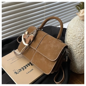 Detail view of caramel brown suede handbag featuring white stitching and horse charm