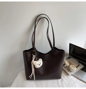 Detail of dark brown tote bag featuring a plush bear charm and metallic hardware accents
