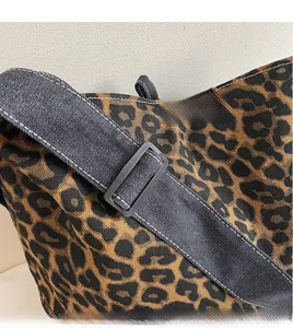 Détail de la bandoulière en denim réglable et toile léopard du sac fourre-tout