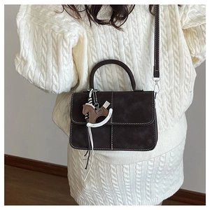 Detail of a dark brown crossbody bag with contrast stitching and a cute horse charm