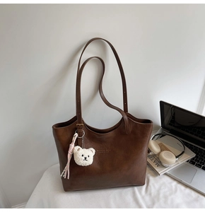 Brown leather tote bag featuring golden brand logo with cute plush bear and tassel charms